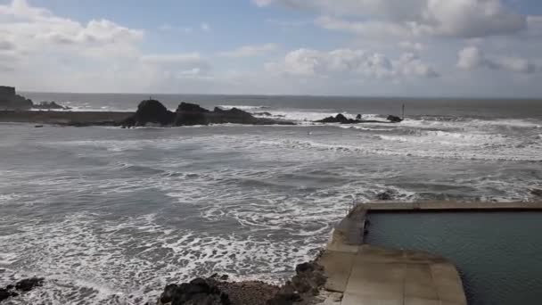 Bude North Cornwall England UK pohjoiseen Boscastle tuulisena päivänä aaltojen ja surffaajien ja suosittu surffauspannulla — kuvapankkivideo