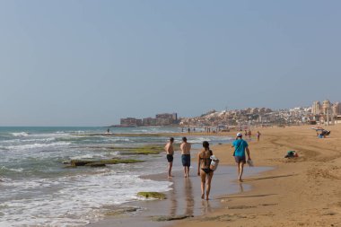Tatilciler ve ziyaretçiler 26 Haziran 2019 Çarşamba günü Torrevieja yakınlarındaki La Mata 'daki güzel plajda yürüyüş yapıyorlar.