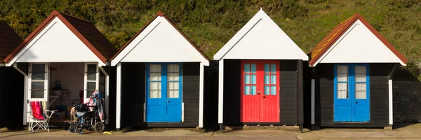 Wheelchair and colourful beach huts with blue and red doors in a row traditional English structure and shelter found at the seaside panorama