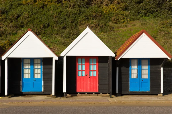 Tři barevné plážové chatky s modrými a červenými dveřmi v tradiční anglické struktury řádku a přístřeší na moře — Stock fotografie