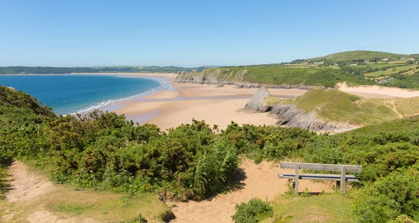 Pobbles praia O Gower Península País de Gales Reino Unido destino turístico popular e ao lado de Três falésias Bay no verão com céu azul e mar Imagens De Bancos De Imagens