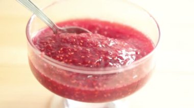 Ahududu reçeli cam bir kaba konur. Ahşap arka planda şekerli ahududu reçeli. Ahududu reçeli cam bir kaba konur..