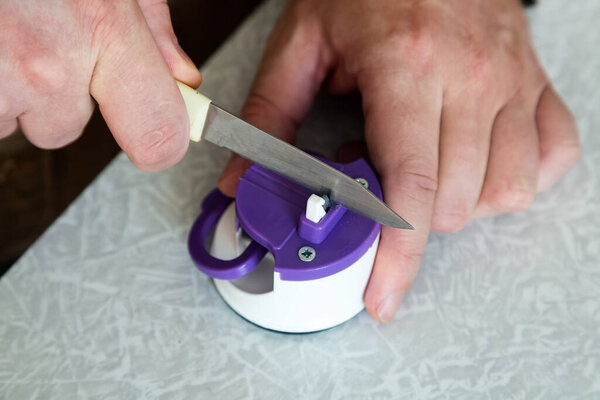 Man sharpens kitchen knife with a sharpener on the table