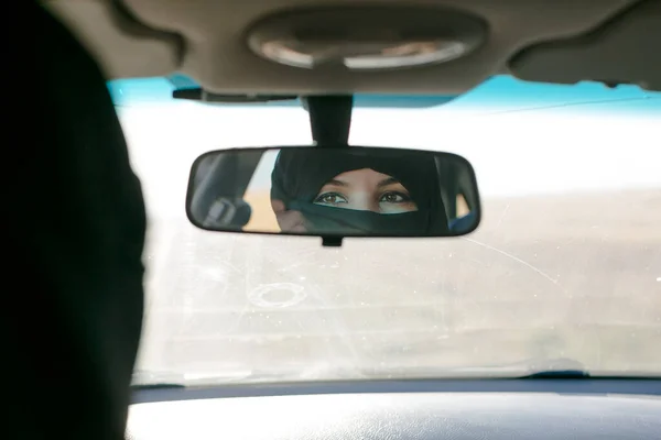 Brunette muslim woman in the reflection of the car mirror in the salon.