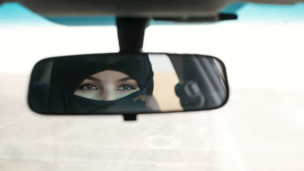 Brunette muslim woman in the reflection of car mirror in the salon.