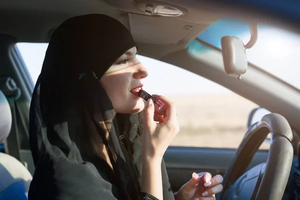 Muslim woman with lipstick in a car, traditional clothes.