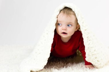 Kafkasyalı yarım yaşındaki bir çocuk kafasını battaniyenin altında saklayan bir oyuncakla oynuyor..