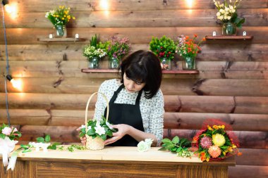 Siyah önlüklü bir işçi sepetinde çiçek ve sabun buketi yapar..