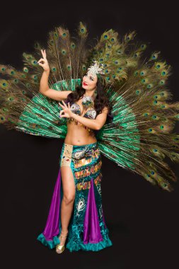 Kafasında tüyler olan esmer bir kadın. Arka planda gür tavus kuşu tüyleri var..