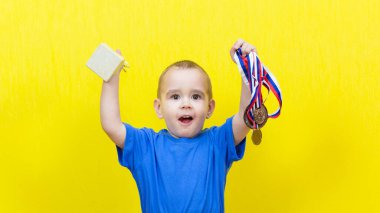 Küçük çocuk, sarı arka planda spor ödüllerine seviniyor..