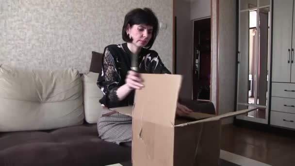 女性は家でソファに座っている間に商品と小包を開きます — ストック動画
