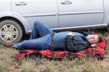 Yorgun sürücü arabanın yanında dinleniyor..