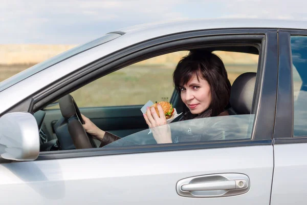 Kobieta Jedzeniem Ręku Prowadzi Samochód — Zdjęcie stockowe