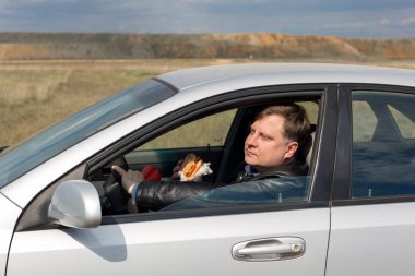 Elinde hamburgerle araba süren mutlu bir adam işe gider..