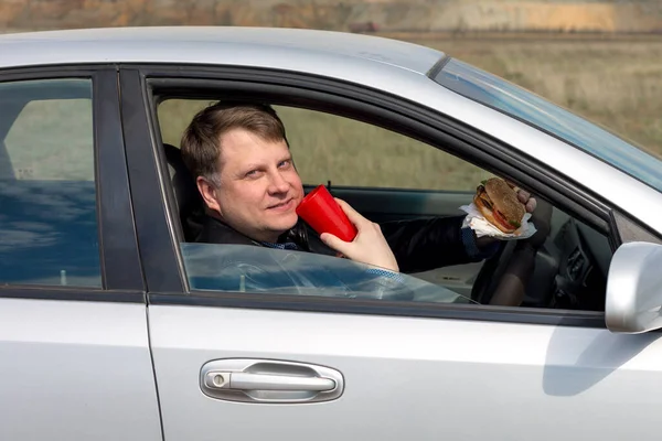 Ευτυχισμένος Άντρας Οδηγεί Ένα Αυτοκίνητο Ένα Ποτήρι Και Ένα Χάμπουργκερ — Φωτογραφία Αρχείου