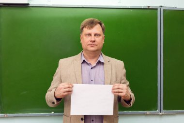 Yeşil tahta kopyalama boşluğunda beyaz kağıtlı katı öğretmen.