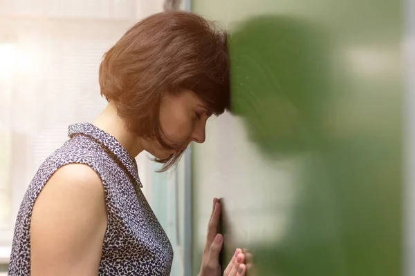 The tired teacher lowered her head and rested forehead on the blackboard.