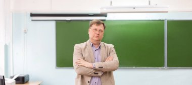 Ciddi müdür, tahtadaki sınıfta kollarını kavuşturmuş duruyor..