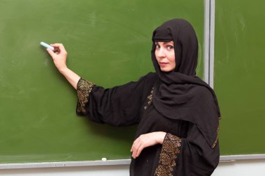 Müslüman bir öğretmen tahtaya tebeşirle yazar..