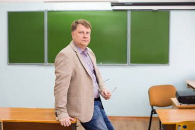 Tahtada elini masaya koyan bir erkek öğretmen öğrencinin cevabını dinler..