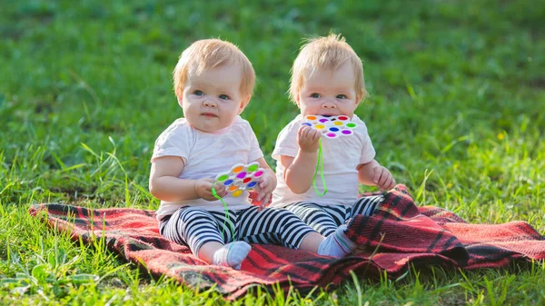 二つの双子の女の子遊びます色のおもちゃと毛布上の晴れた夏の日 — ストック写真