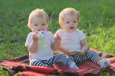 Kardeş bebekler parktaki çimenlerin üzerinde aileleri olmadan otururlar..
