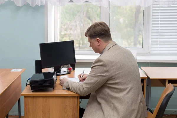 A professor at the institute at his desk by the window writes assignments for his students.