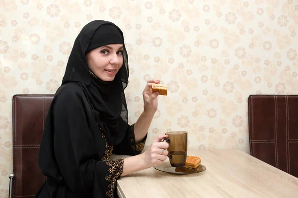 一位穿着民族服装的穆斯林妇女正在公寓的餐桌边吃早餐 — 图库照片
