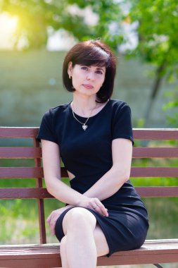 Siyah elbiseli yorgun bir esmer işten sonra parkta bankta dinleniyor..