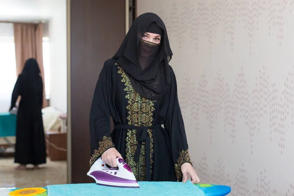 一名身穿民族服装的穆斯林妇女在公寓里熨烫衣服 — 图库照片