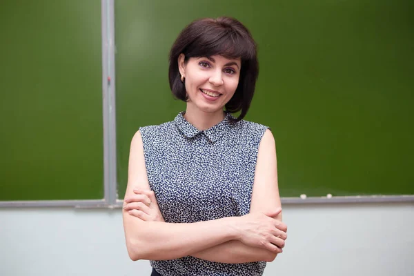 Mavi bluzlu gülümseyen bir öğretmen sınıfın tahtasında duruyor..