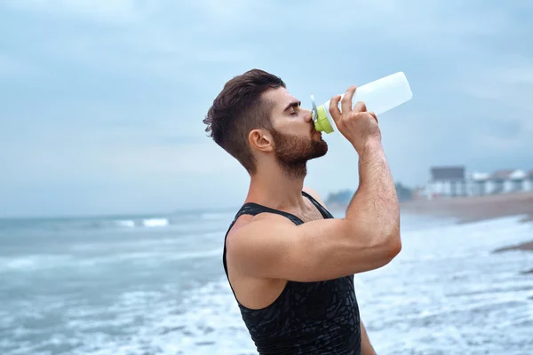 Homem bebendo água refrescante após o treino na praia. Beba. — Fotografia de Stock
