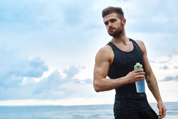 Homem da aptidão com a garrafa de água que descansa após o exercício na praia — Fotografia de Stock