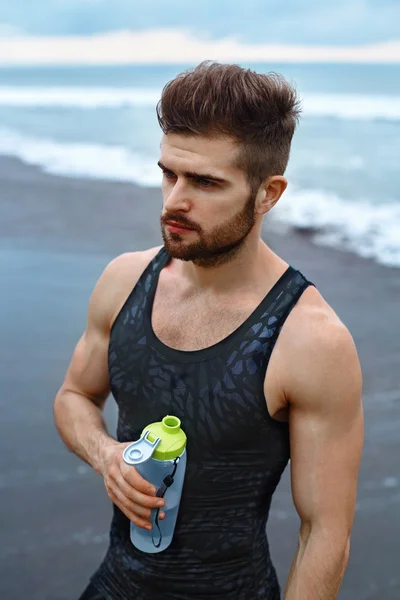 Homem bebendo água refrescante após o treino na praia. Beba. — Fotografia de Stock