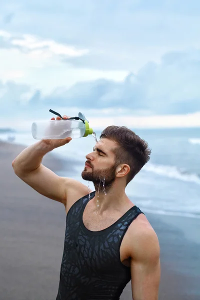 Hombre deportivo vertiendo agua sobre la cara después del entrenamiento en la playa . — Foto de Stock