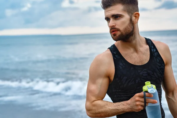 Mann trinkt erfrischendes Wasser nach dem Training am Strand. Trinken — Stockfoto