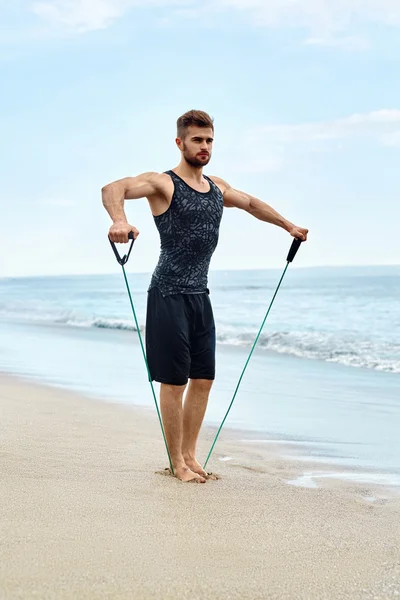 Deportes. Hombre haciendo ejercicios de expansor al aire libre en la playa. Entrenamiento corporal — Foto de Stock