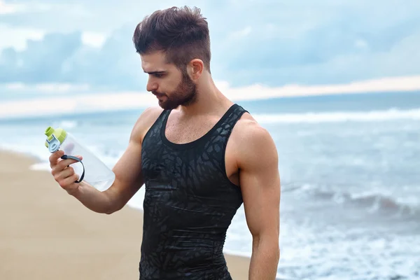 Fitnessmann mit Wasserflasche ruht nach dem Training am Strand — Stockfoto