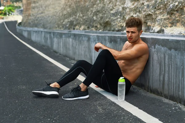 Hombre deportivo cansado descansando después de correr y hacer ejercicio al aire libre — Foto de Stock