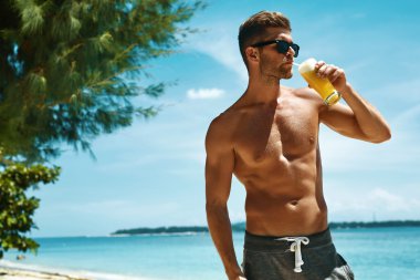 Kaslı vücutlu adam sahilde sağlıklı içki içiyor. Yaz