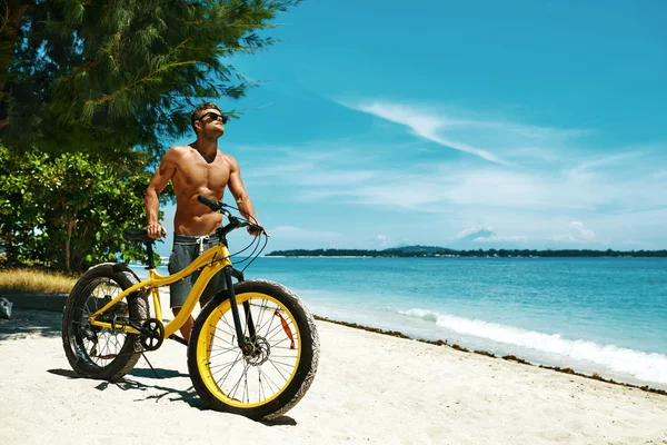 Knappe man met fiets zon looien op het strand. Zomervakantie. — Stockfoto
