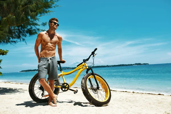 Hombre guapo con bicicleta sol bronceado en la playa. Vacaciones de verano . — Foto de Stock