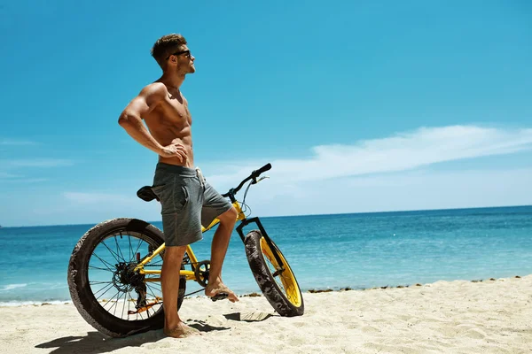 Homem bonito com bicicleta sol bronzeando na praia. férias de verão . — Fotografia de Stock