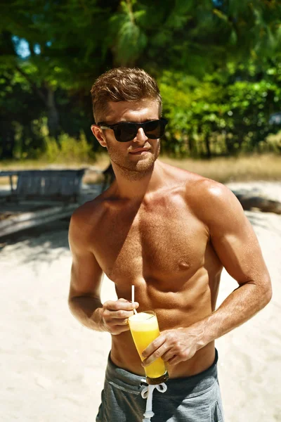 Sommaren. Atletisk muskulös man dricker juice cocktail på stranden — Stockfoto