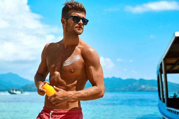 Hombre bronceado usando Sun Block Body Cream en la playa de verano —  Fotos de Stock