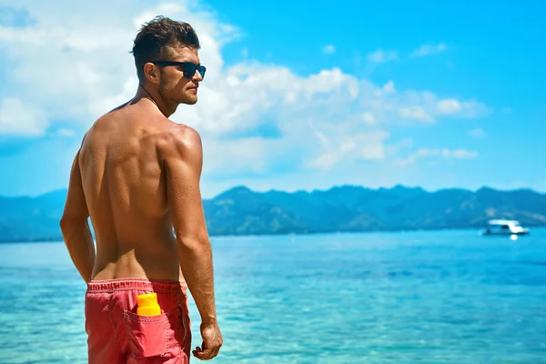 Sexy man looien met sunblock huid crème op zomer strand. — Stockfoto