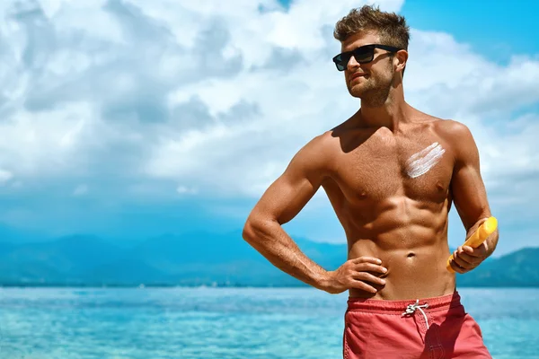 Sexy hombre bronceado usando crema protector solar en la piel del cuerpo. Verano —  Fotos de Stock
