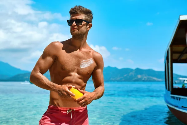 Man Tanning Using Sun Block Body Cream On Summer Beach