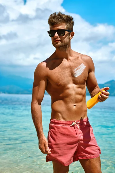 Homem sexy bronzeando usando protetor solar creme na pele do corpo. Verão — Fotografia de Stock