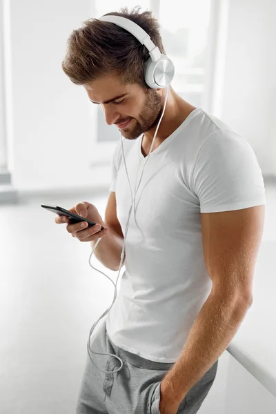 Homem ouvindo música em fones de ouvido usando telefone celular dentro de casa — Fotografia de Stock